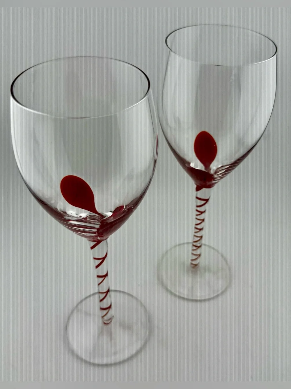 2 Pier 1, red ribbon swirl stem wine glasses, w/ a red swirl design on the stem.